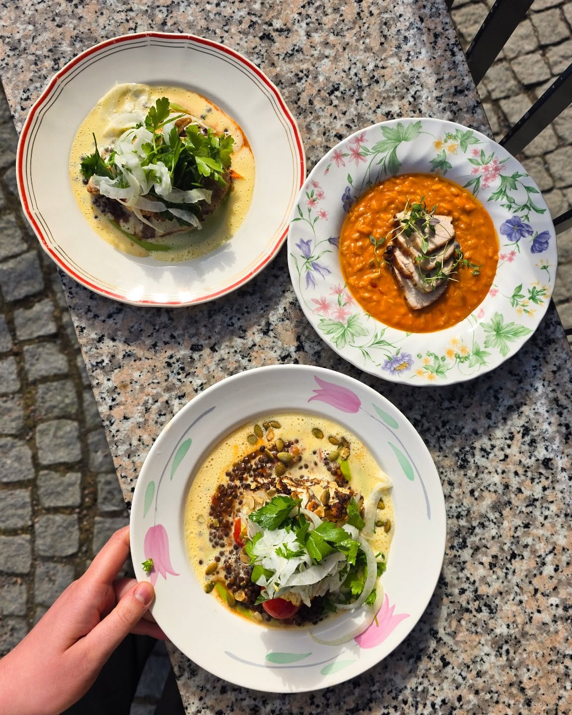 Three bowls of soup on a granite table: top-left beef in pale cream sauce with greens and onions, top-right orange lentil soup with sliced meat, bottom bowl with creamy lentil topping and seeds.