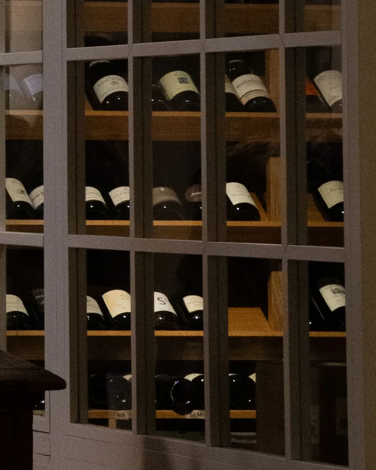 Rows of wine bottles stored on wooden shelves behind glass doors in a wine cabinet.