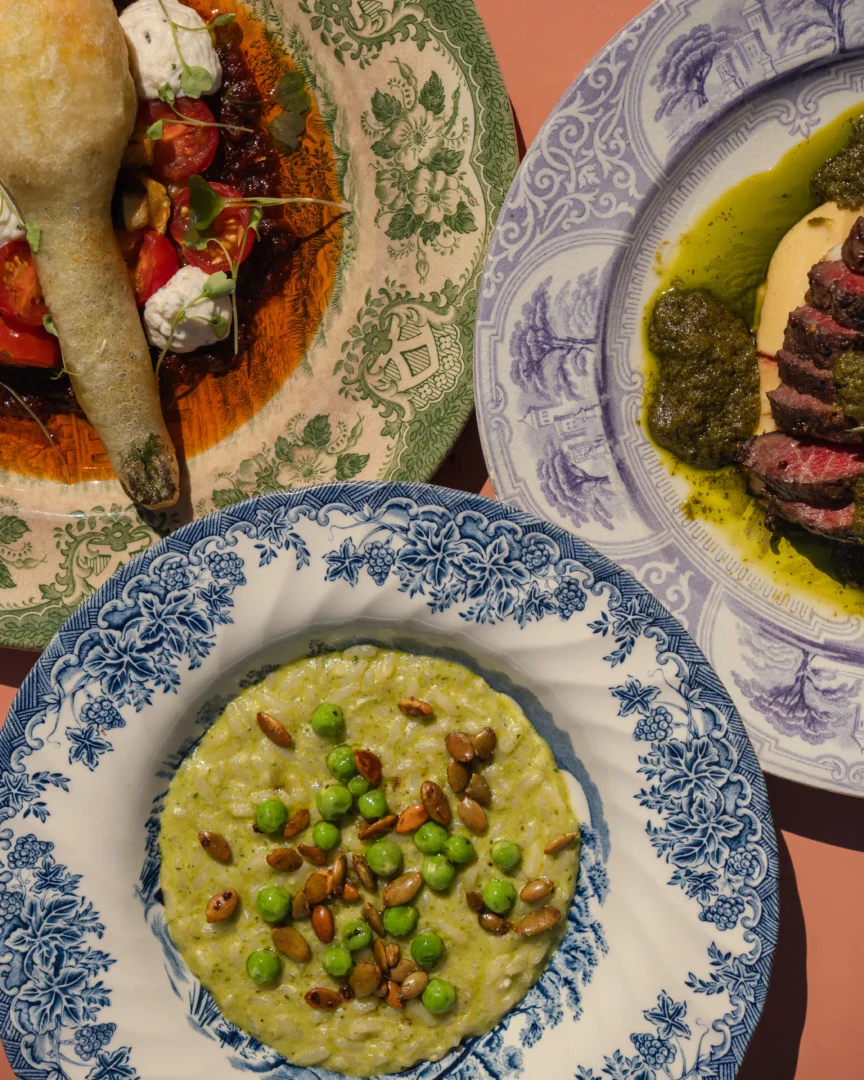 Assorted dishes on patterned plates: creamy risotto with peas and toasted nuts, a bread roll with vegetables, and sliced beef with green sauce.