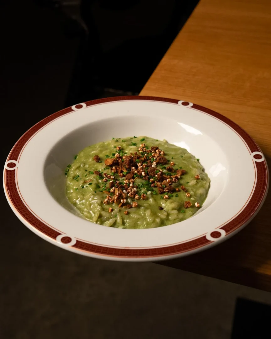 Creamy green risotto with parsley and crunchy nuts on a white plate with red rim