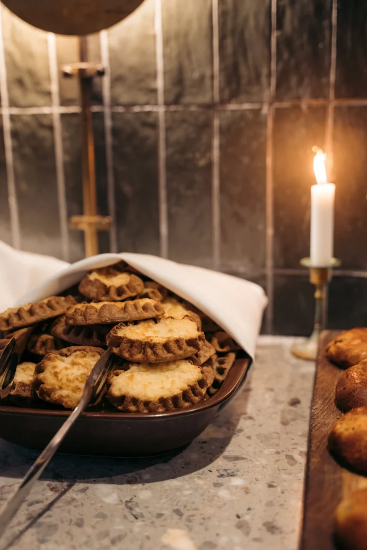 Tray of baked cookies stacked in a serving bowl with a white napkin, on a speckled counter, candlelit background.
