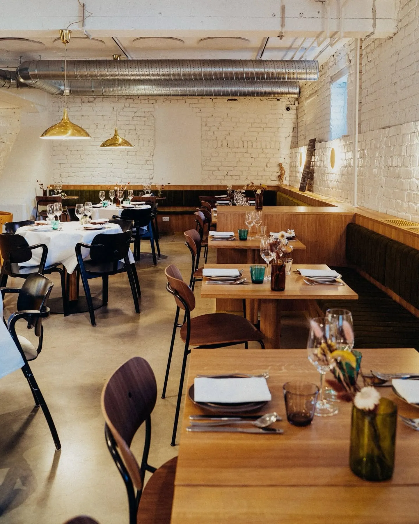 Industrial-style restaurant interior with white brick walls, wooden tables set for dining and gold pendant lights overhead.