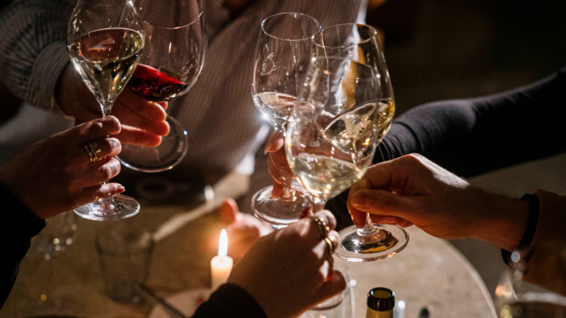 Group of people clinking wine glasses around a candlelit dinner table.