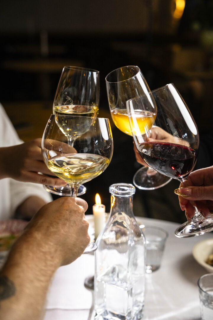 Group of people clinking wine glasses at a candlelit dinner table on toast.