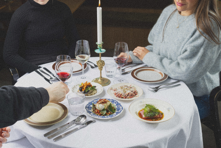 Kolme asiakasta Ravintola Albinan valkoisella pöytäliinalla katetun pöydän ääressä, useita gourmet-ruokalajeja, valko- ja punaviinilaseja, kultainen kynttilänjalka keskellä pöytää luomassa intiimin fine dining -tunnelman